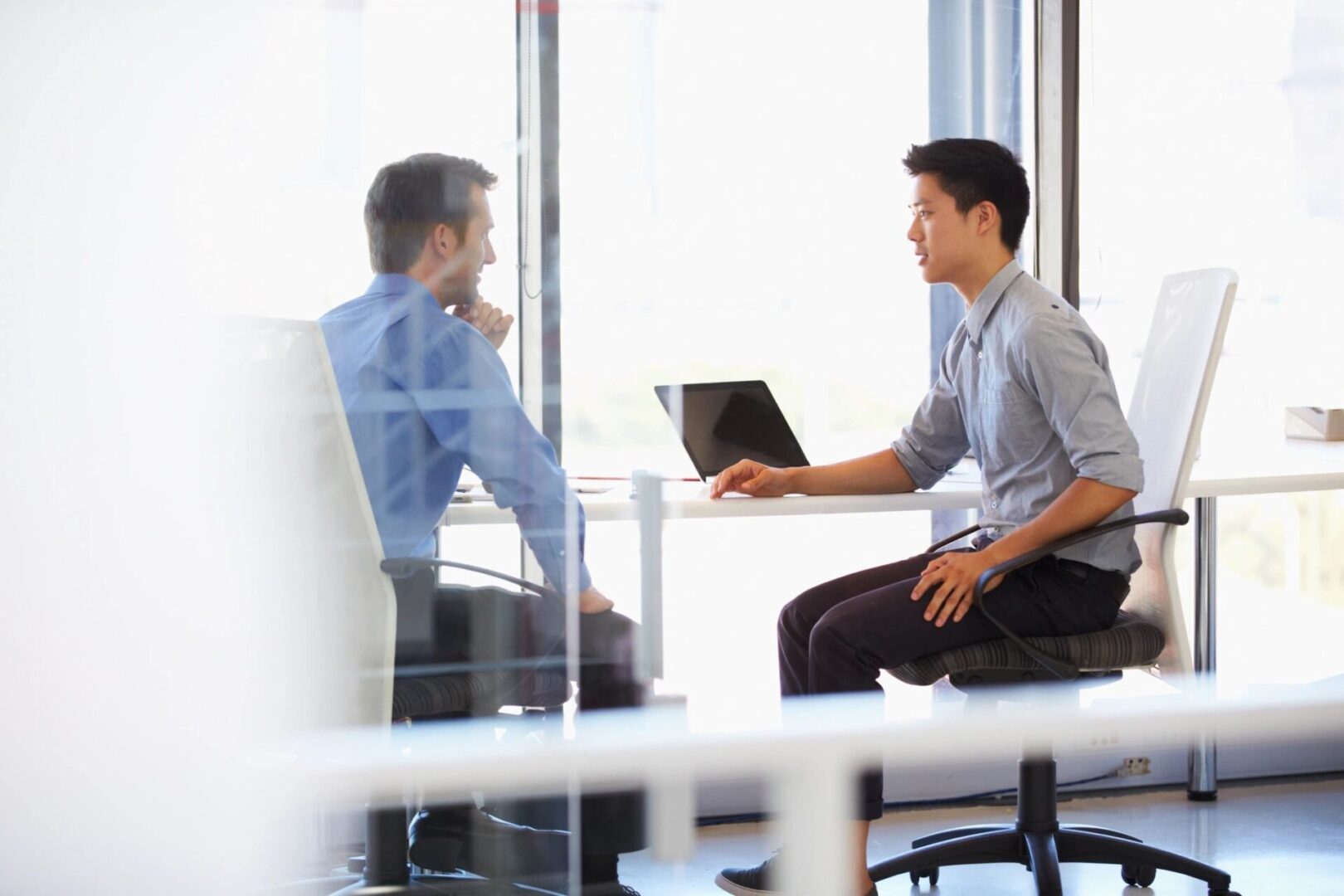 Two men are sitting at a table with laptops.